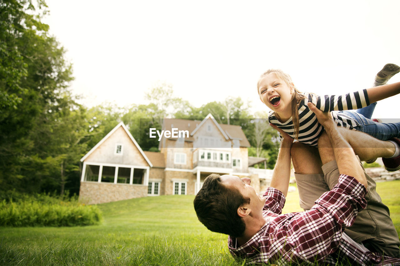 Playful man playing with daughter in backyard against sky