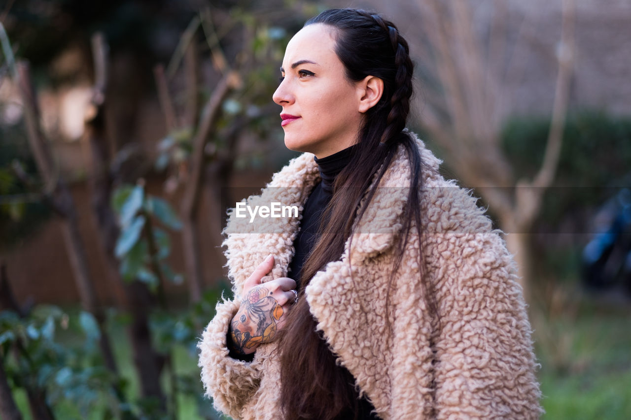 YOUNG WOMAN LOOKING AWAY WHILE STANDING OUTDOORS