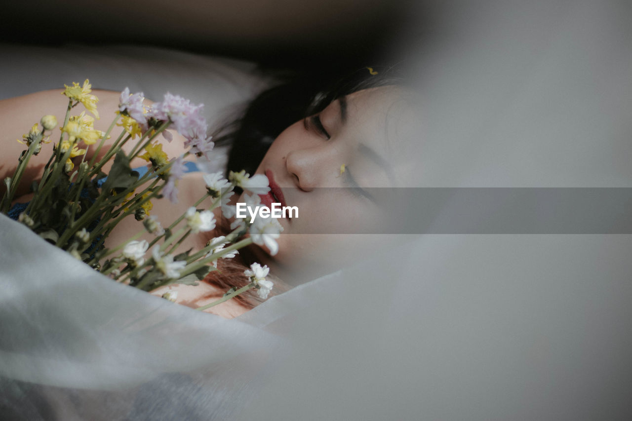 High angle view of woman holding bouquet while sleeping on bed at home