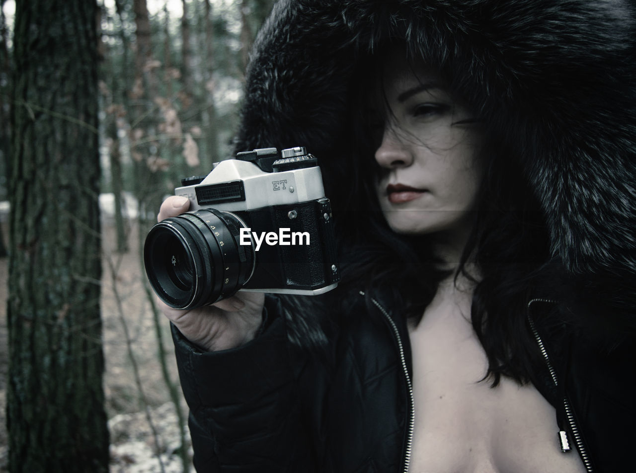 Beautiful fashion model holding camera in forest