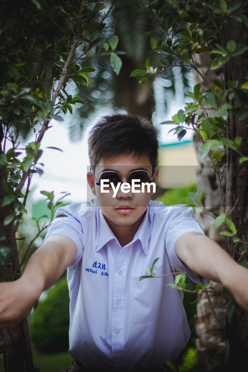 Portrait of young man wearing upside down sunglasses by plants