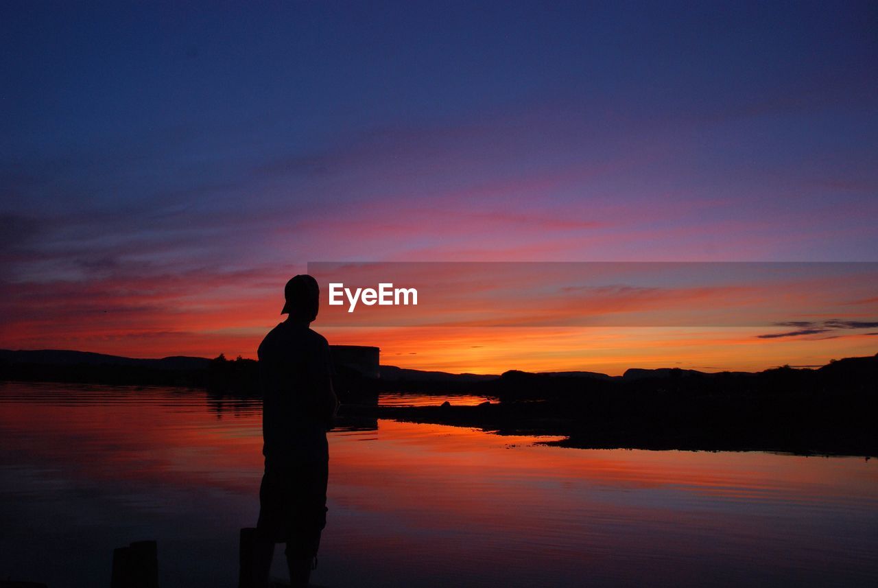 Silhouette man standing at beach against sky during sunset