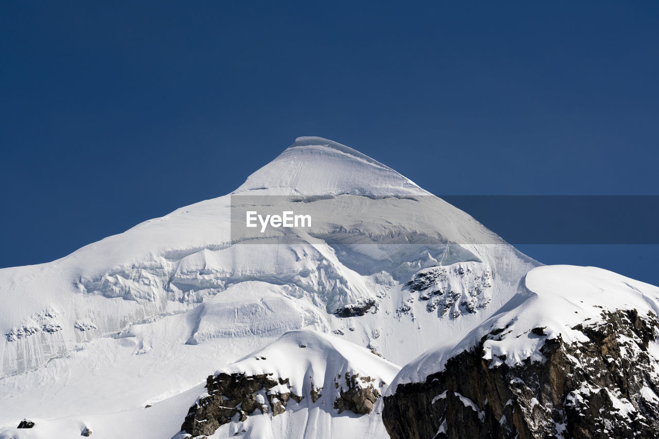 low angle view of snowcapped mountains against clear blue sky