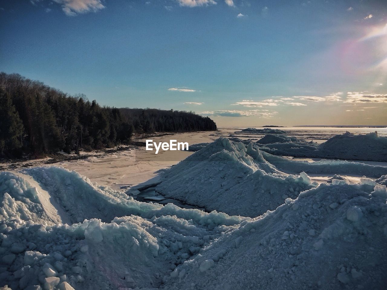Ice stacks on beach with trees against blue sky