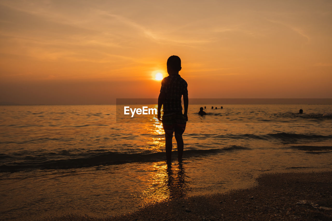 SILHOUETTE MAN STANDING ON BEACH DURING SUNSET