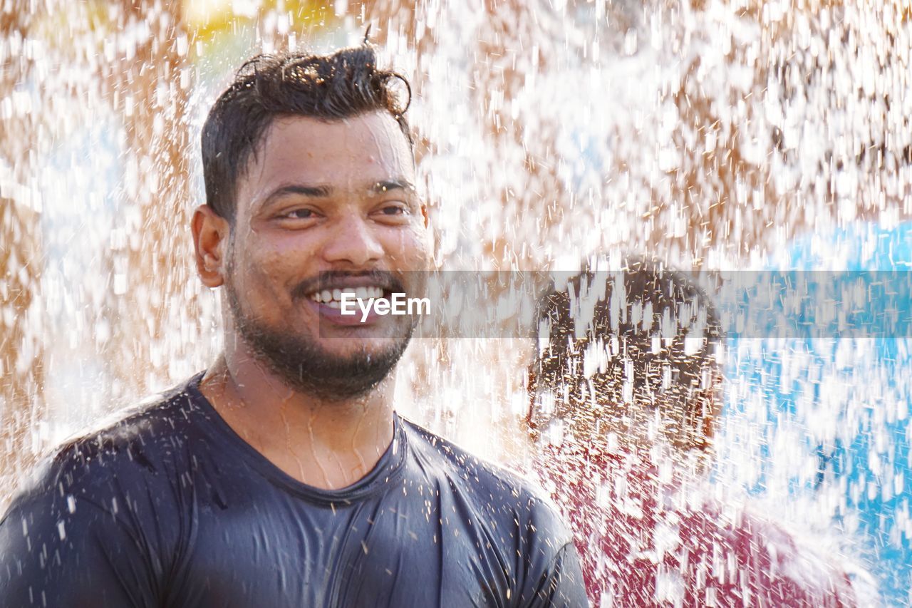 Water splashing on smiling young man 