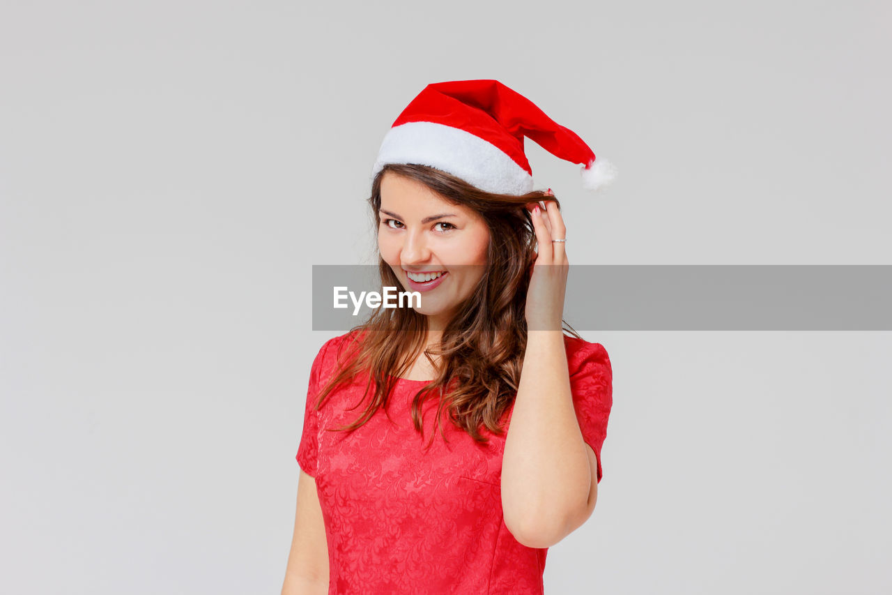 Portrait of happy young woman wearing santa hat while standing against gray background