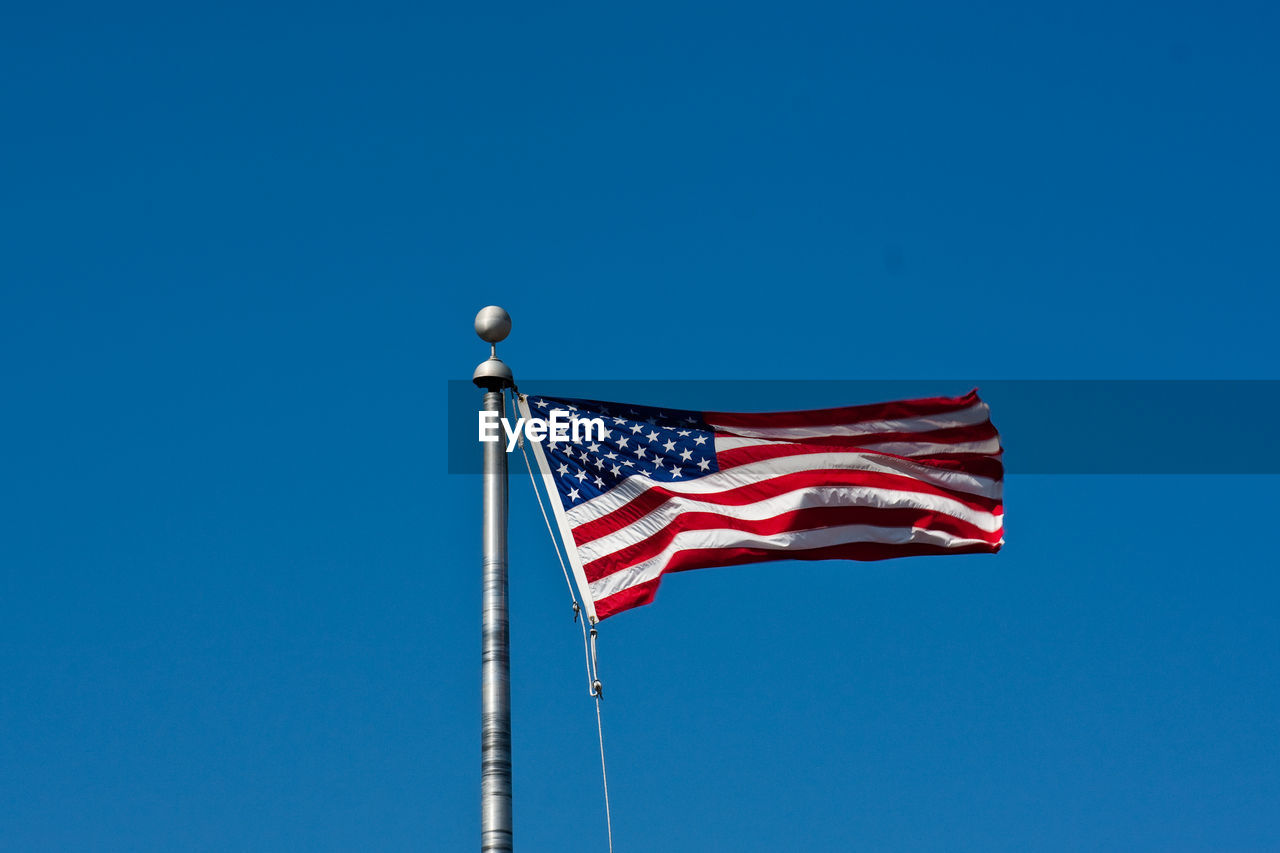 Low angle view of american flag waving against clear blue sky