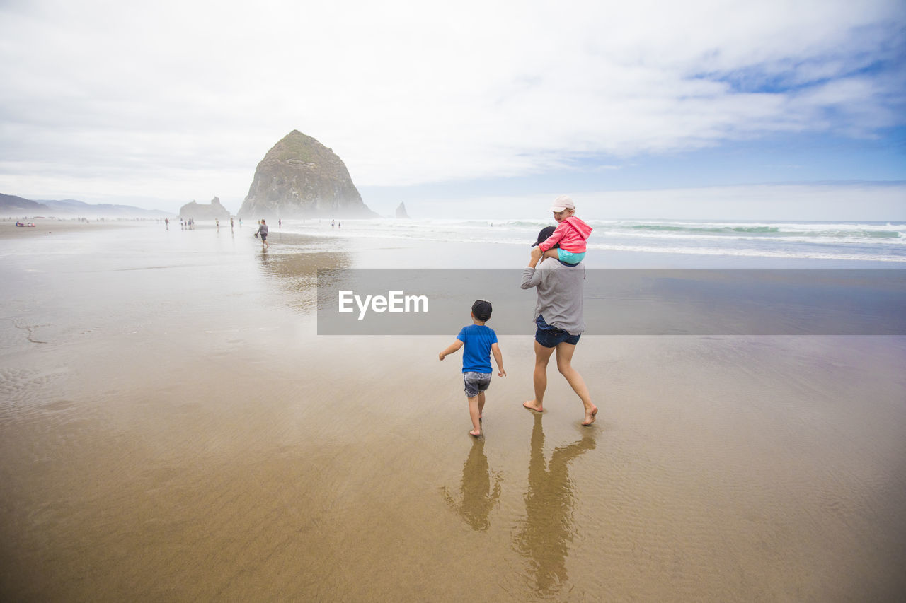 Mother and two kids walk toward haystack rock, cannon beach.