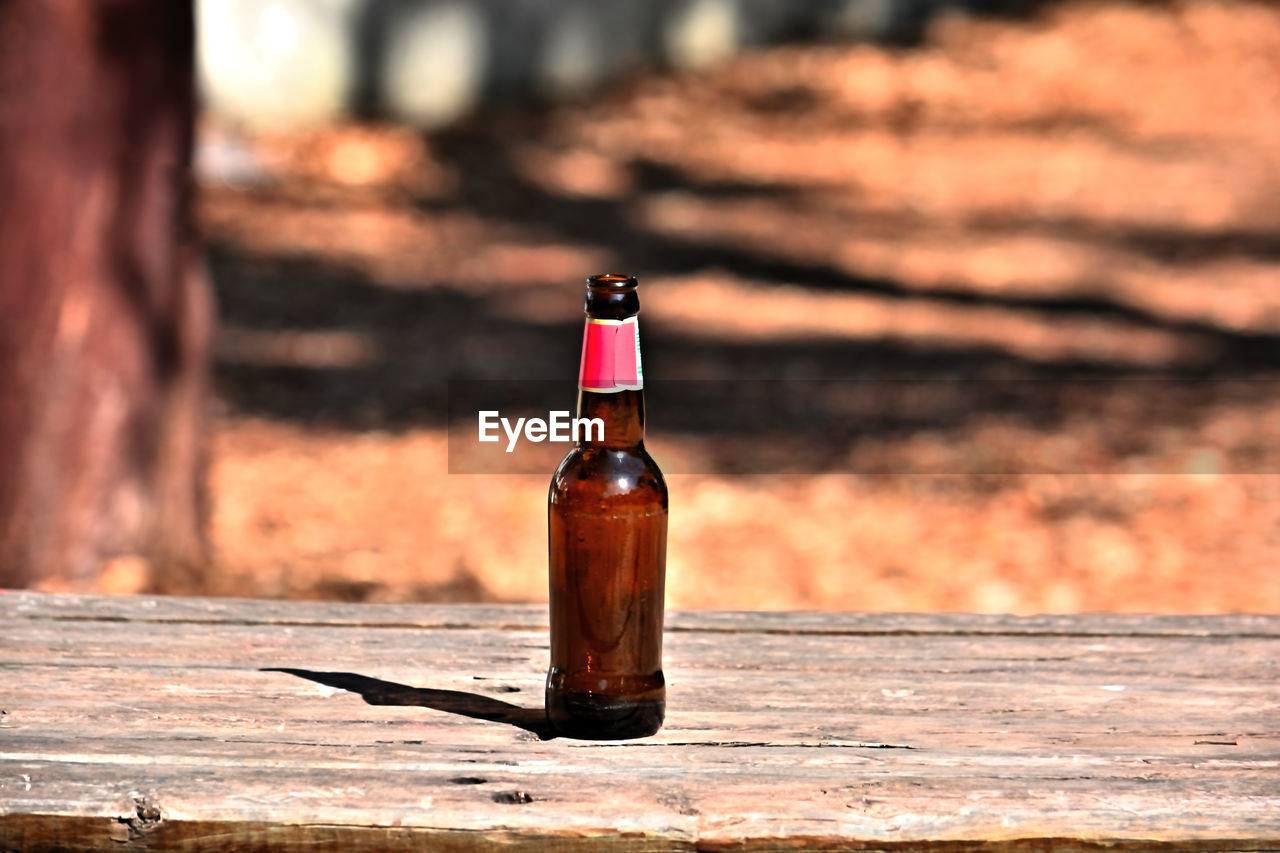 bottle, container, refreshment, wood, food and drink, alcohol, drink, alcoholic beverage, nature, focus on foreground, sunlight, no people, wine bottle, glass, outdoors, wine, beer, table, day, red, food
