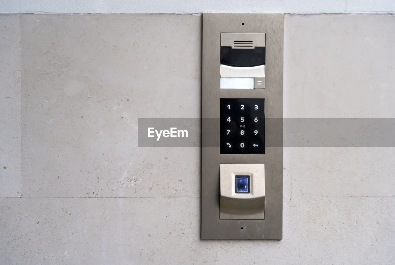 Matte metal intercom call panel with white digital buttons and fingerprint scanner on limestone wall