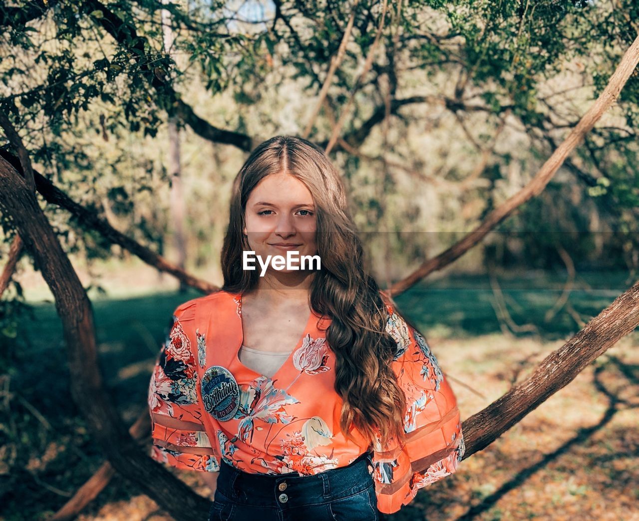 PORTRAIT OF SMILING YOUNG WOMAN STANDING ON TREE