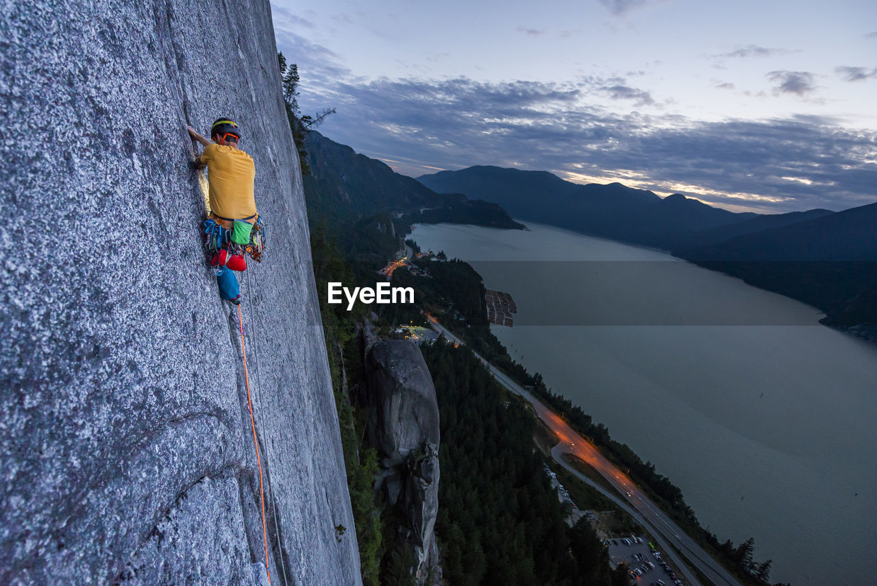 Side view man rock climbing at sunset above the sea and highway