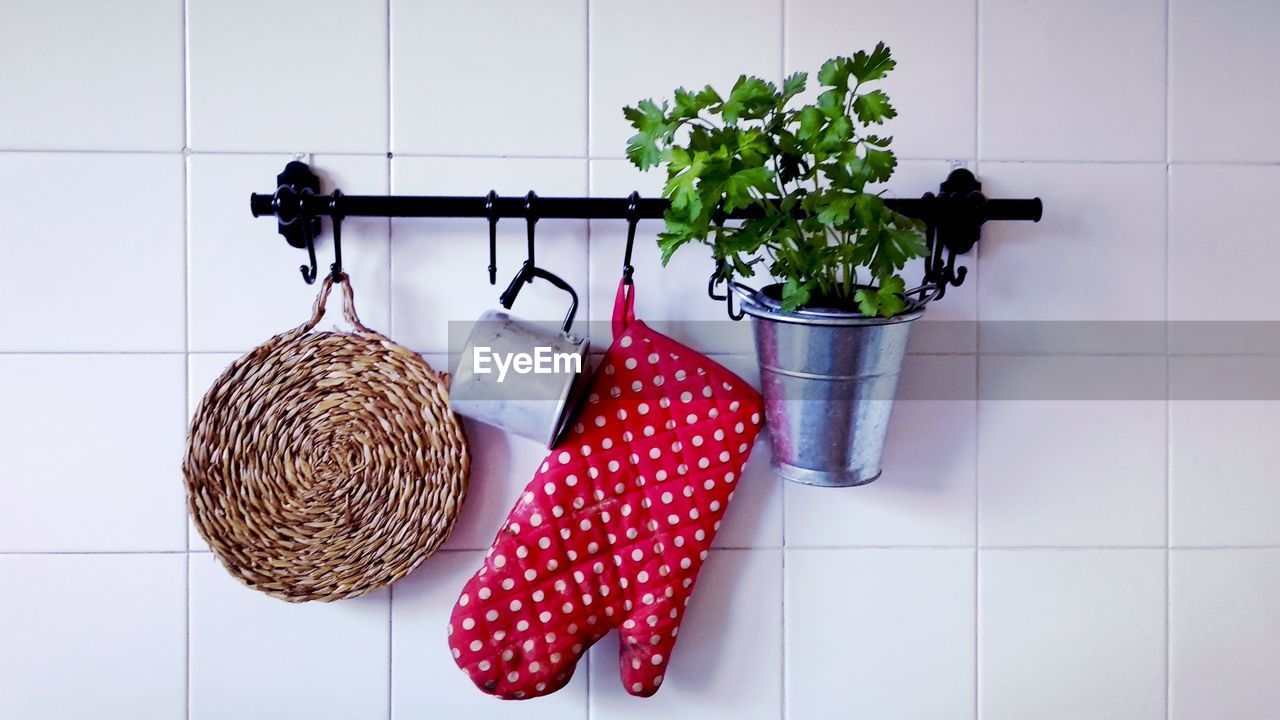 Close-up of oven mitt with potted plant and mug hanging on tiled wall