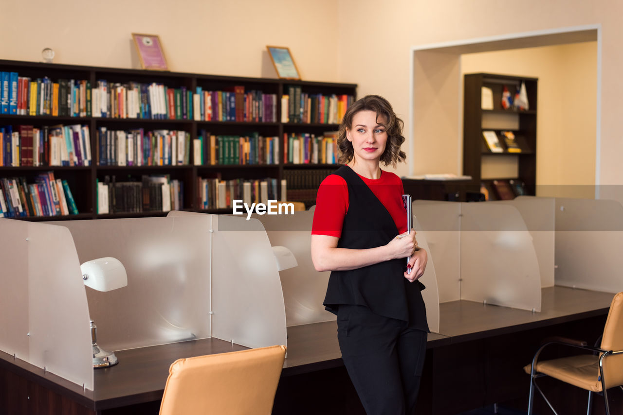 Professional woman educator or manager posing at public library of high school or college