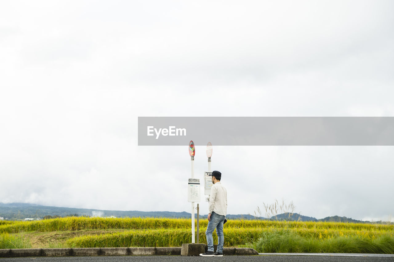 Rear view of man standing at bus stop against sky