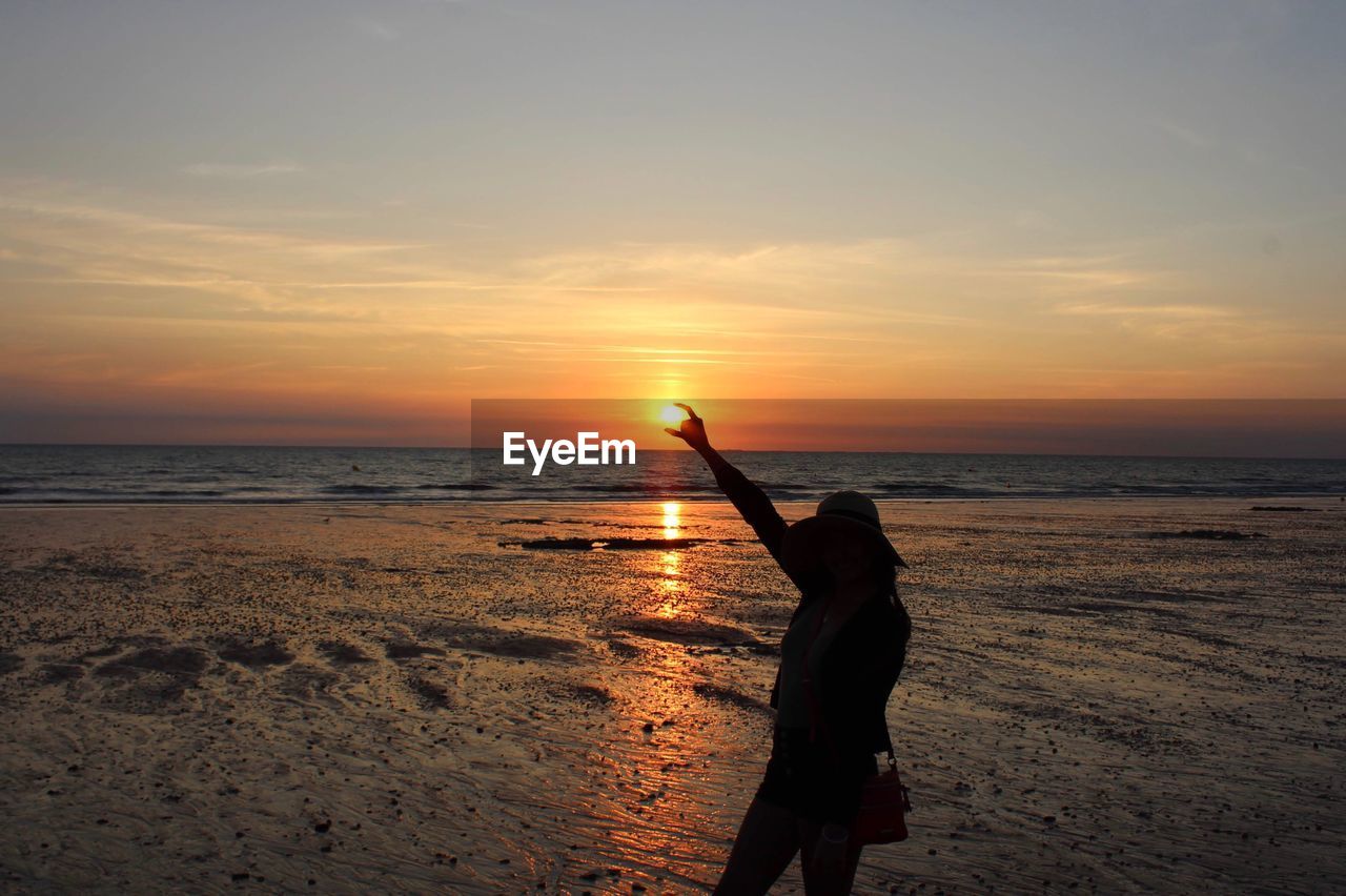 Silhouette woman standing at beach against sky during sunset