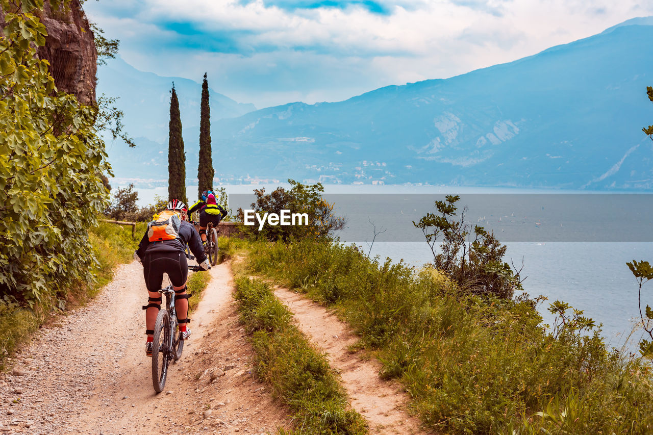 People riding bicycle on dirt road against sky