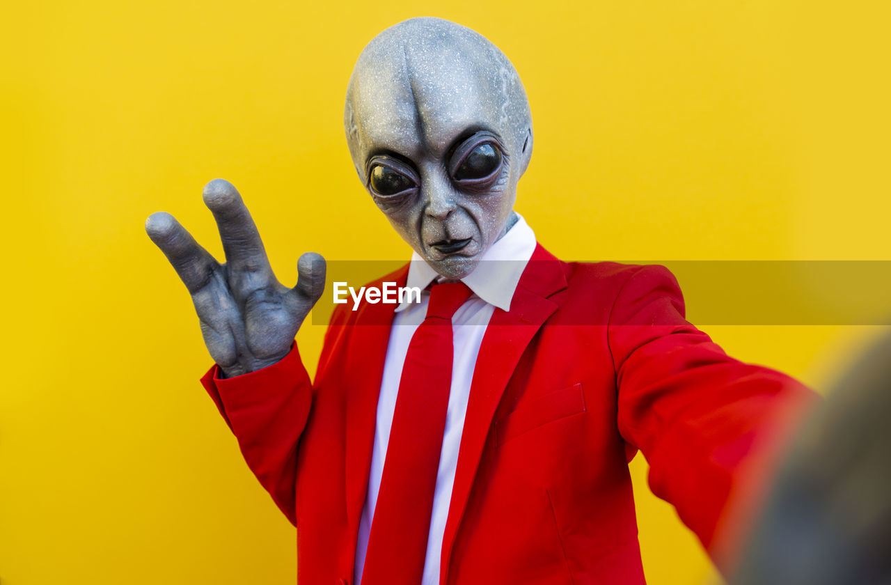 Portrait of man wearing alien costume and bright red suit reaching toward camera