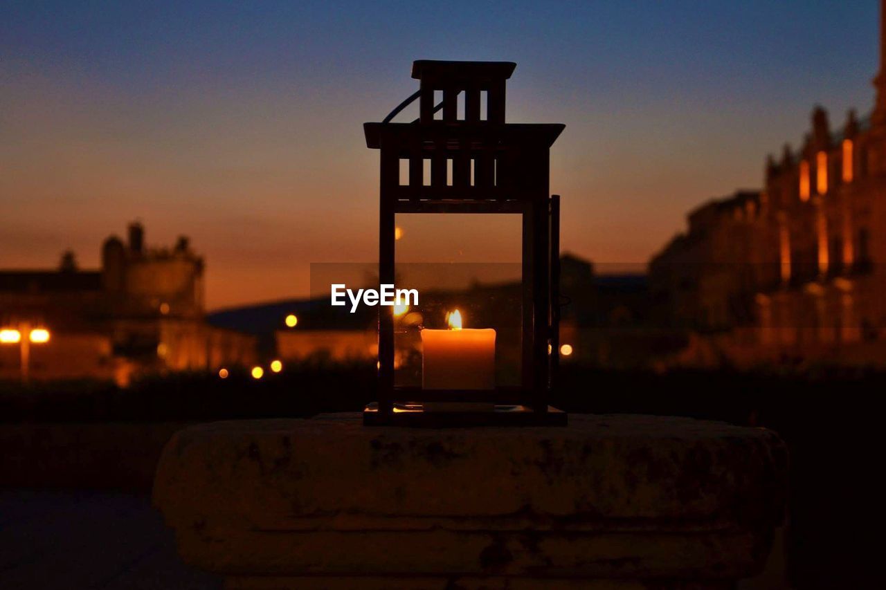 CLOSE-UP OF ILLUMINATED LAMP AT SUNSET