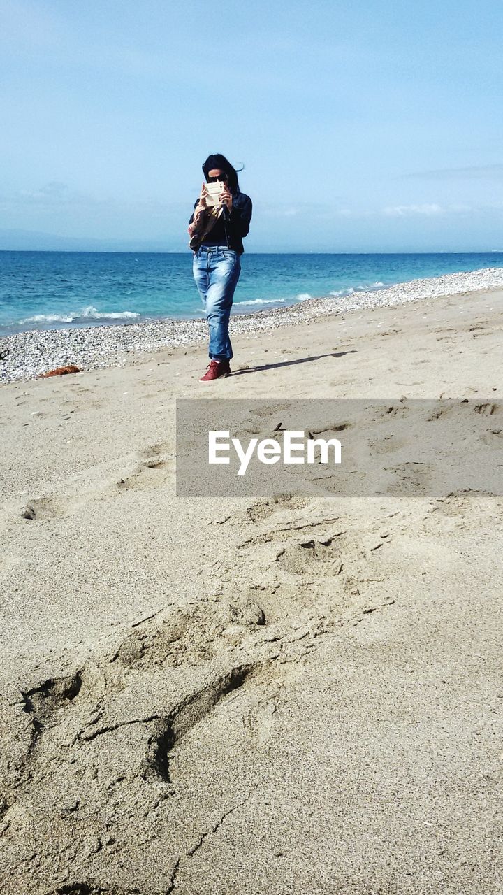 Woman photographing through mobile phone at beach