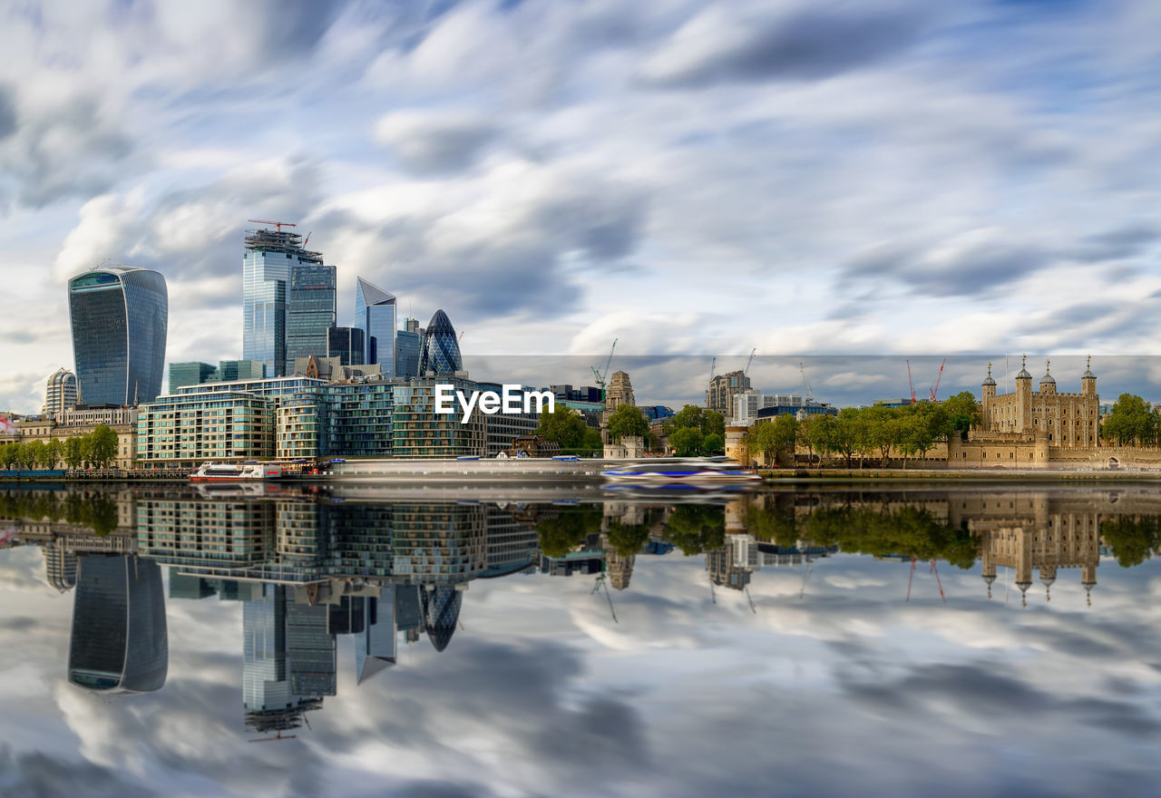 Reflection of buildings on lake against cloudy sky