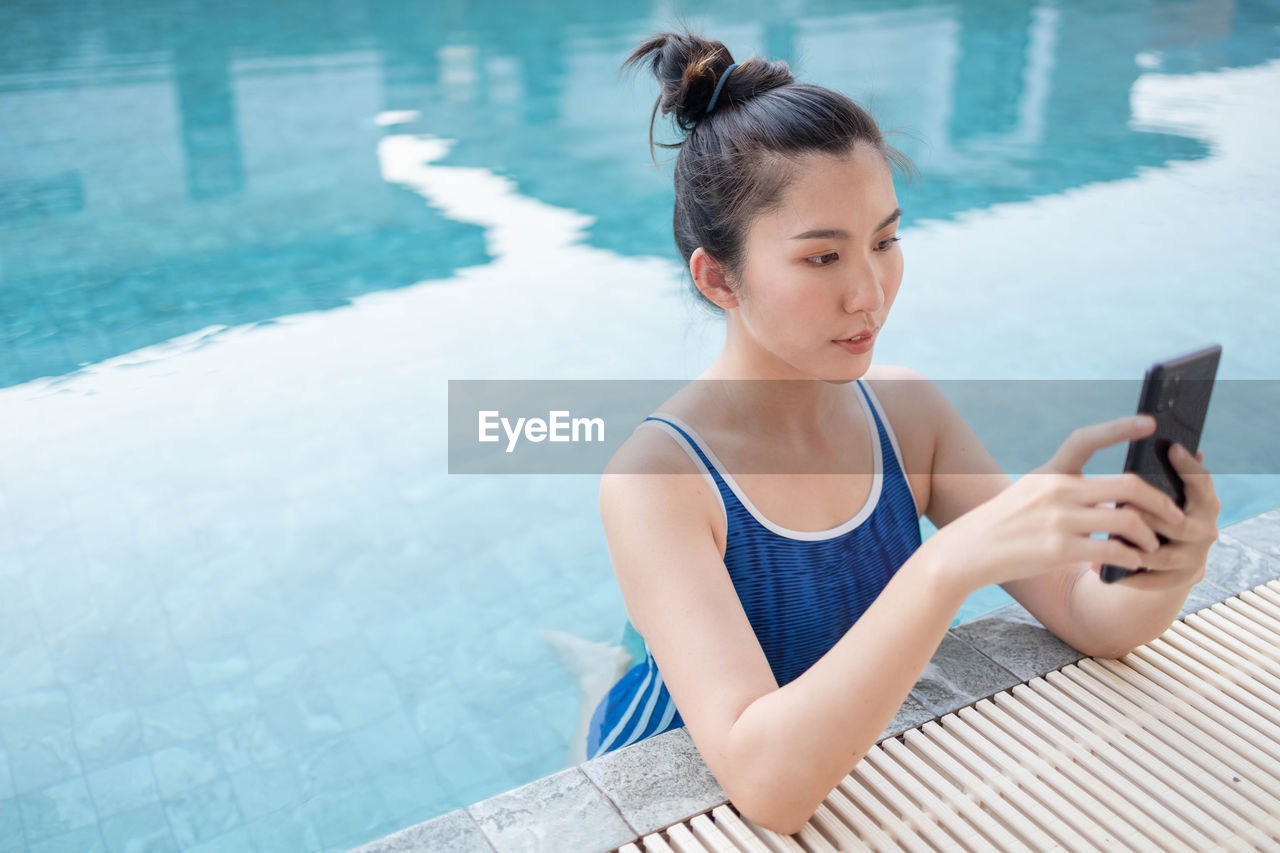 WOMAN USING MOBILE PHONE WHILE SWIMMING POOL