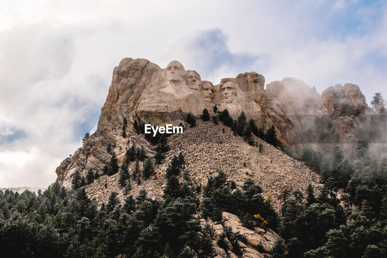 Low angle view of rocks on mountain against cloudy sky