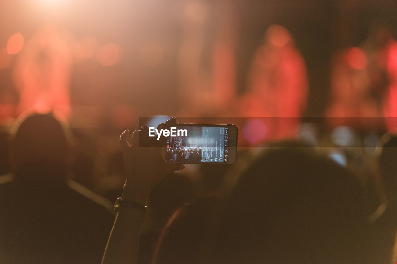 Cropped hands of woman photographing with smart phone at music concert