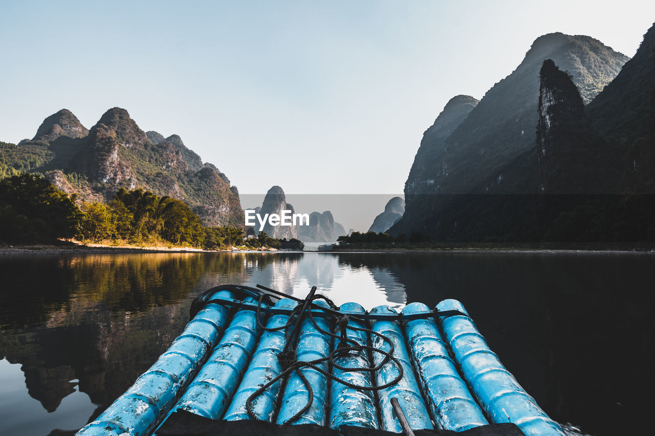 Blue wooden raft in lake with mountains in background against clear sky