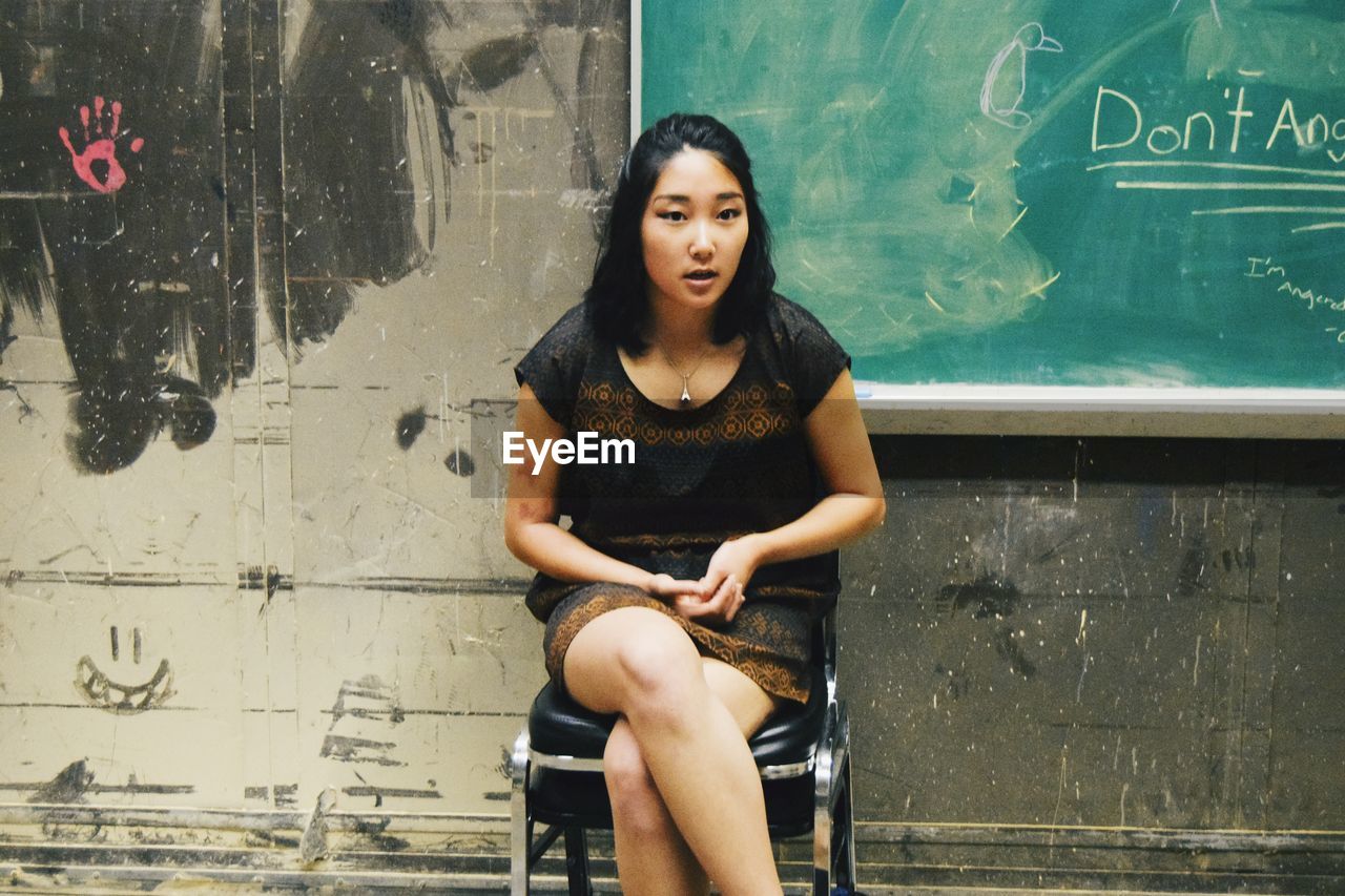 Woman sitting on chair against chalkboard on old wall