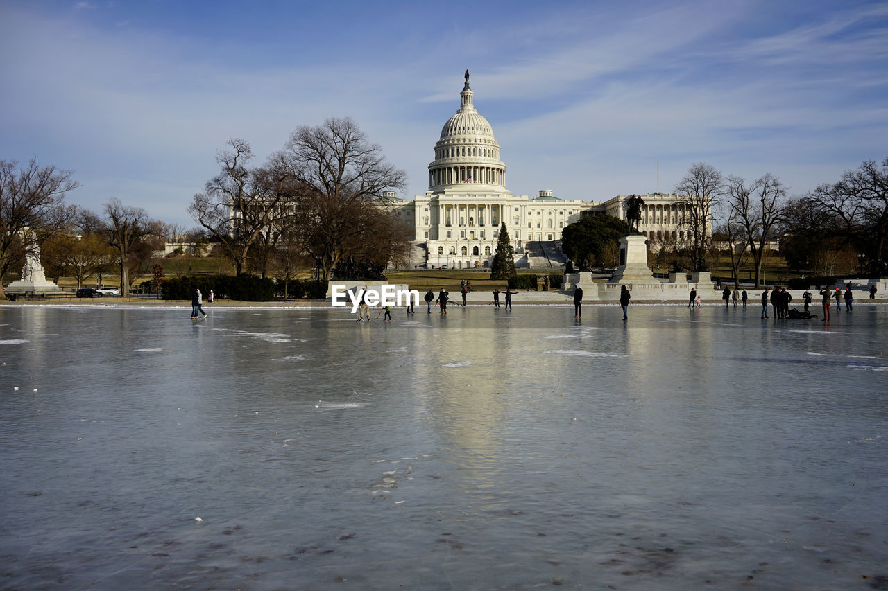 Low angle view of historic capitol, people walking on frozen reflecting pool