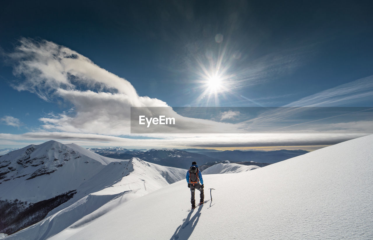 Rear view of mid adult man hiking on snowcapped mountain against cloudy sky