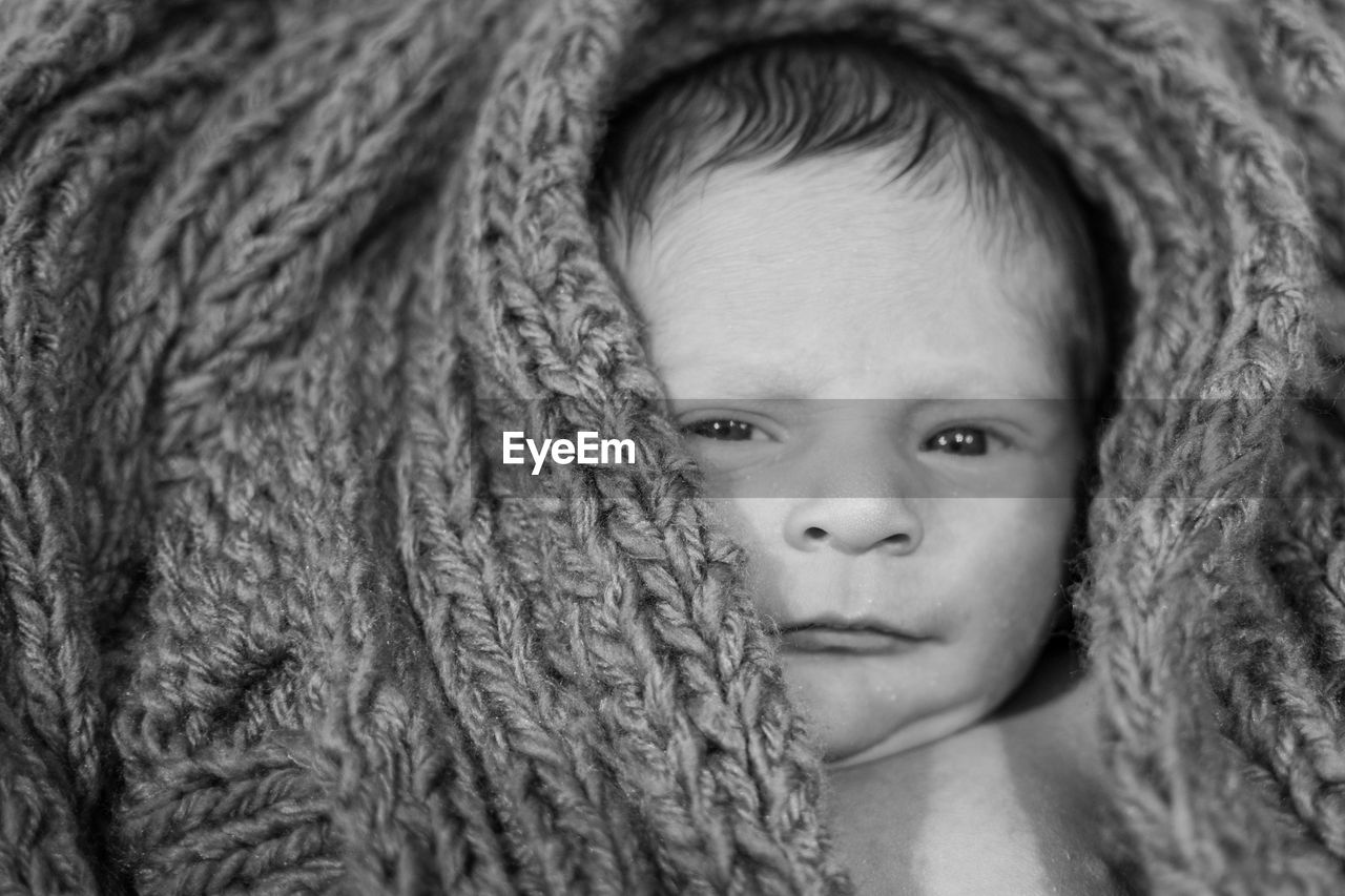 Portrait of cute baby boy lying in knitted wool at home