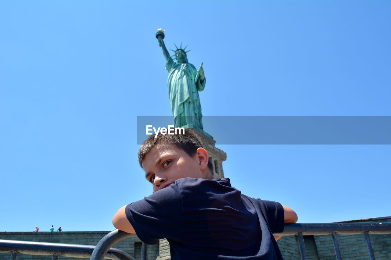 Low angle portrait of boy standing against statue of liberty