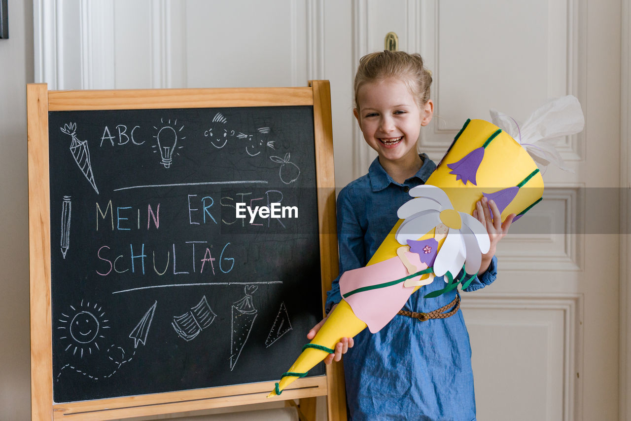 Cheerful girl standing by blackboard at home