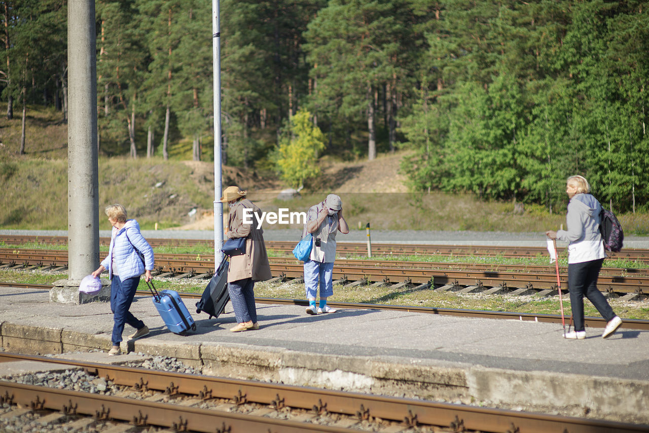 Four old senior women on  platform are waiting for a train and wearing a face mask during a pandemic