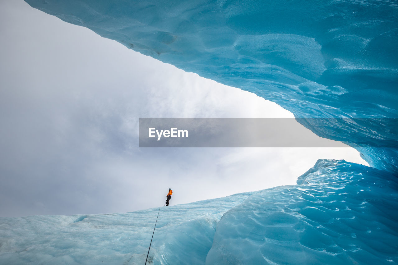 Low angle view of person standing on ice at strupbreen against cloudy sky