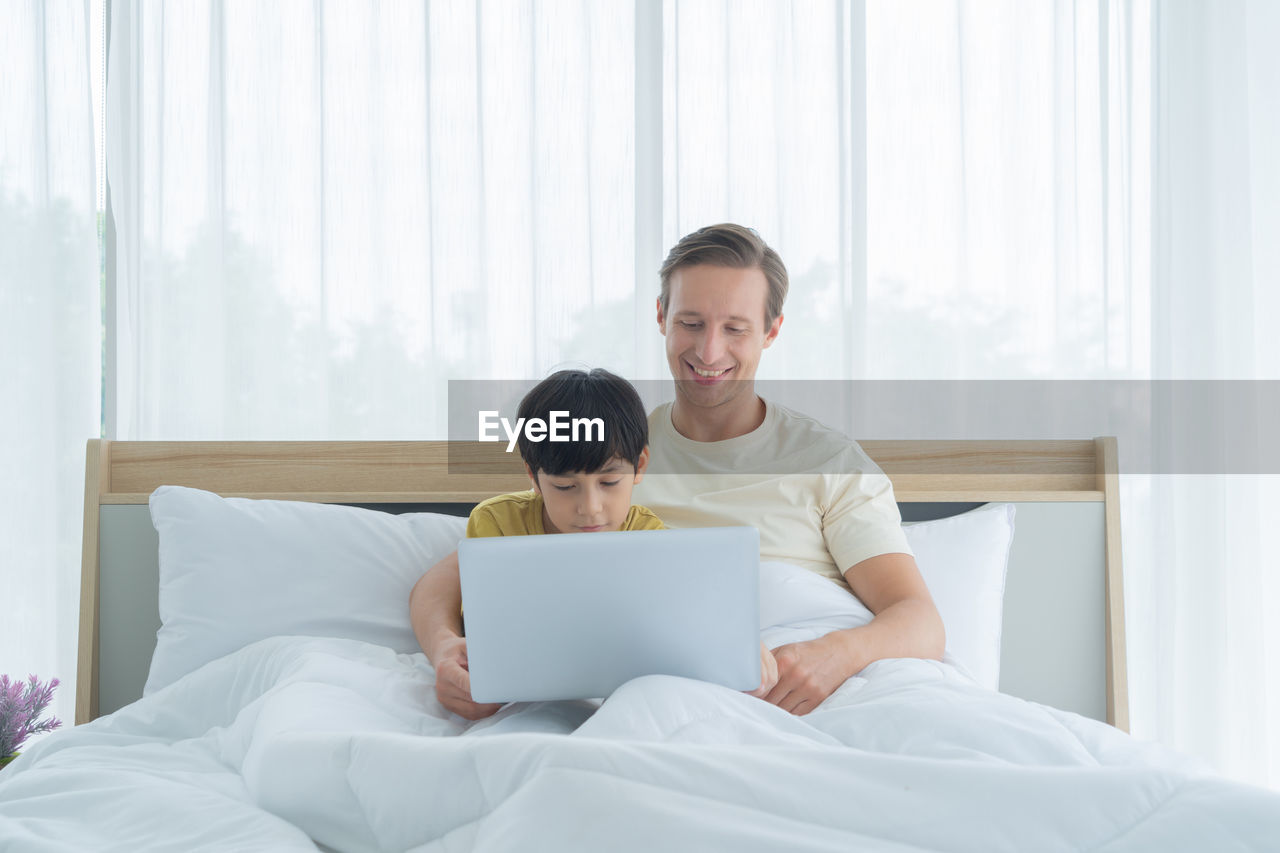 Man and woman using mobile phone while sitting on bed
