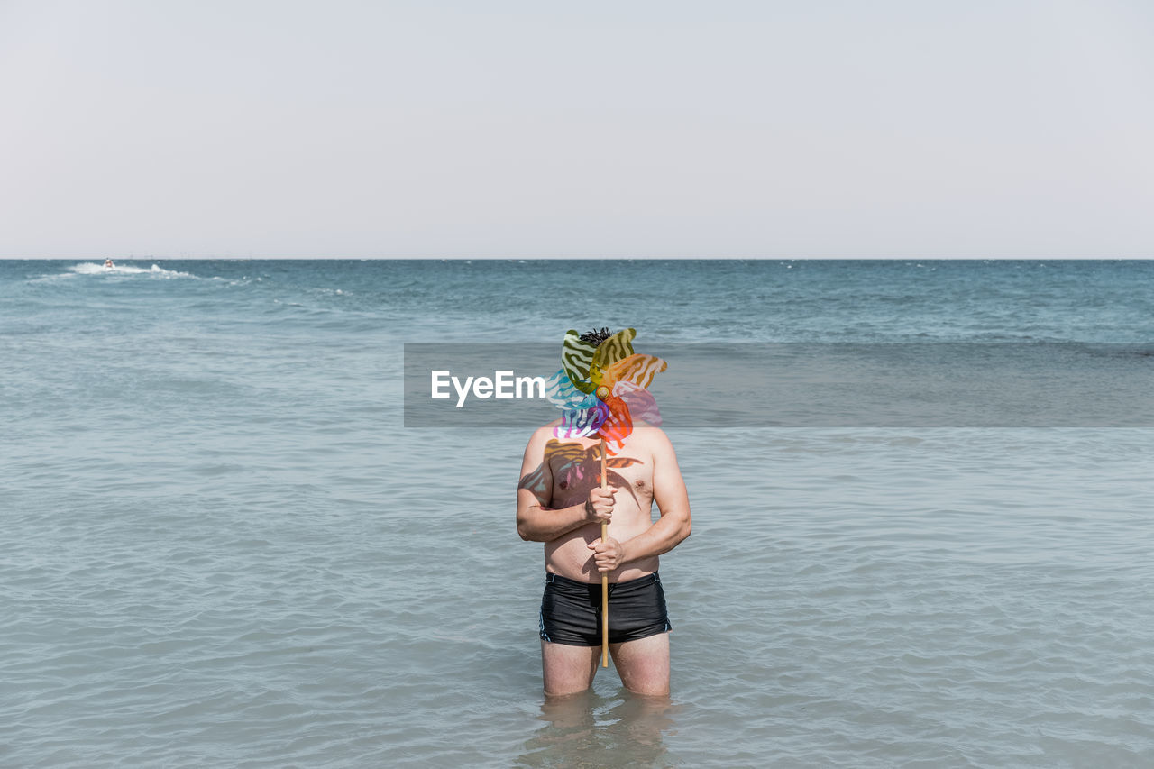 Shirtless man with pinwheel toy standing in sea
