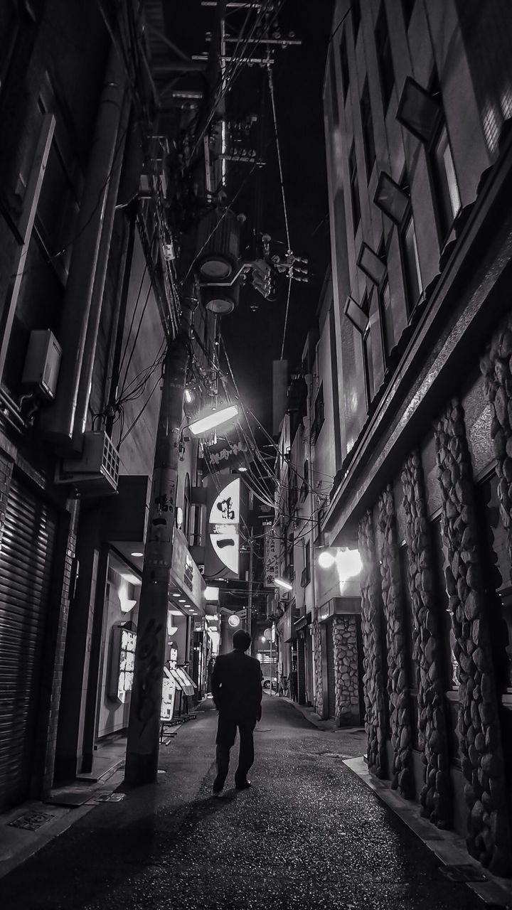 Rear view of man walking in narrow street at night