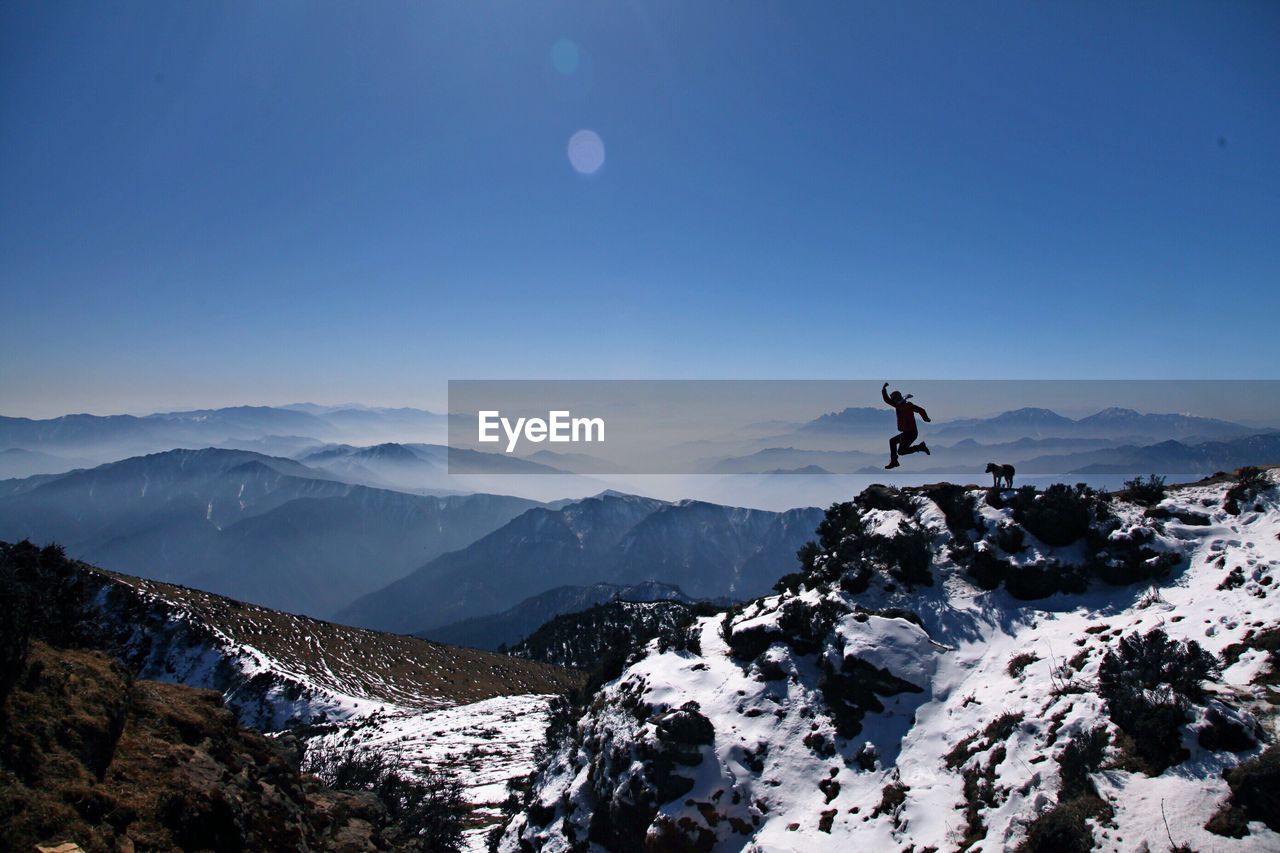 Silhouette man jumping on mountain against clear blue sky during sunny day