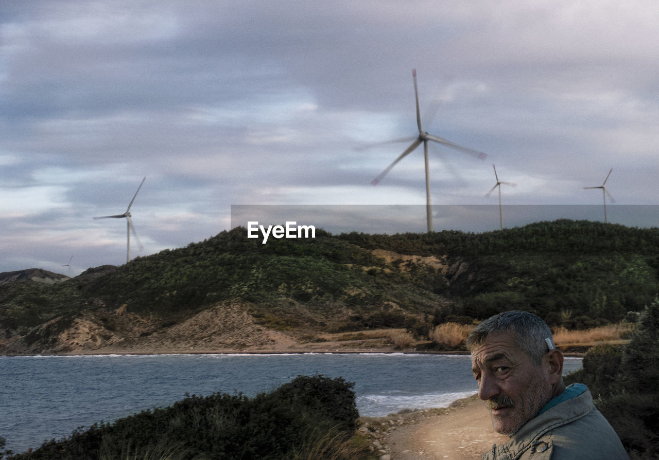 Portrait of man against wind turbines on mountain and lake