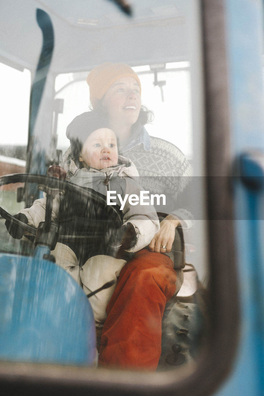 Mother and daughter sitting in tractor seen through windshield