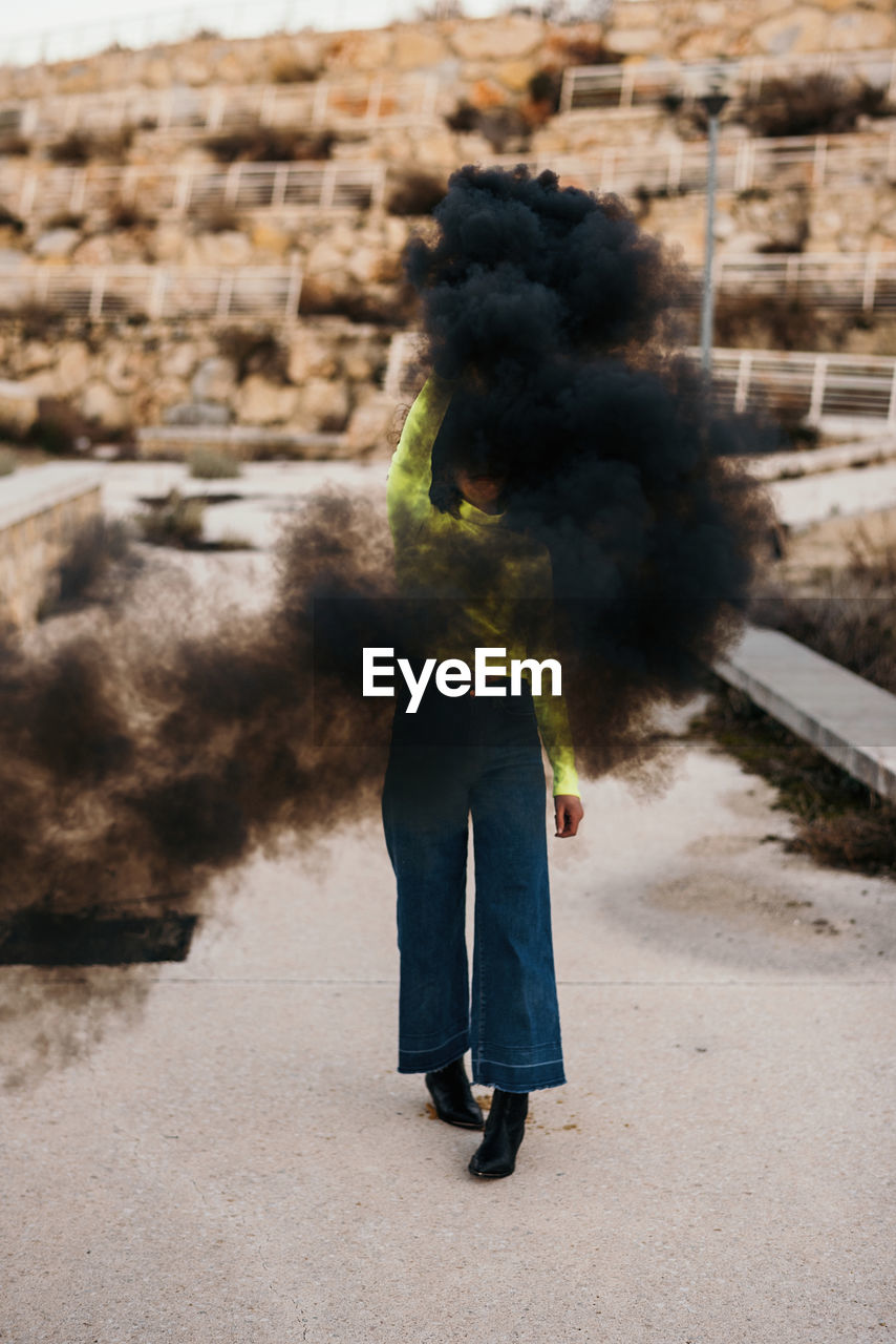 Contemporary unrecognizable lady in trendy wear among black smoke with city on background