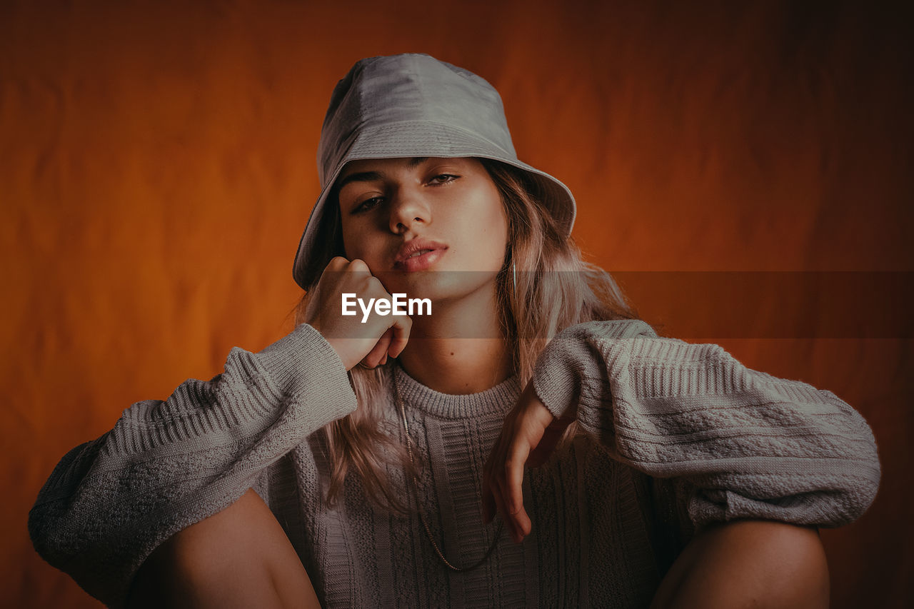 Portrait of young woman in hood clothing against wall