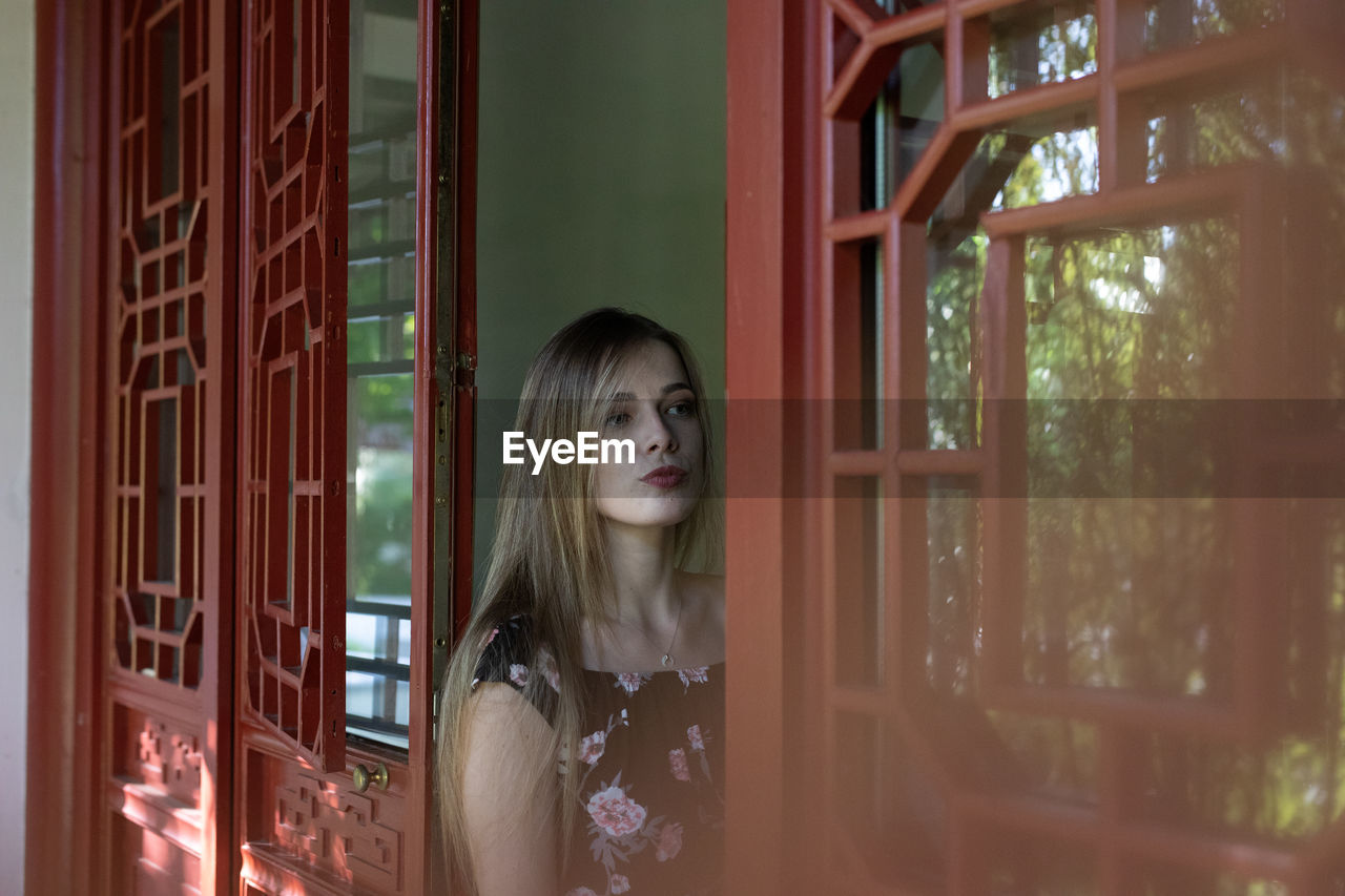 Portrait of woman standing against window at home