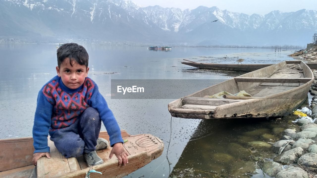 Portrait of boy sitting on boat moored at lake during winter