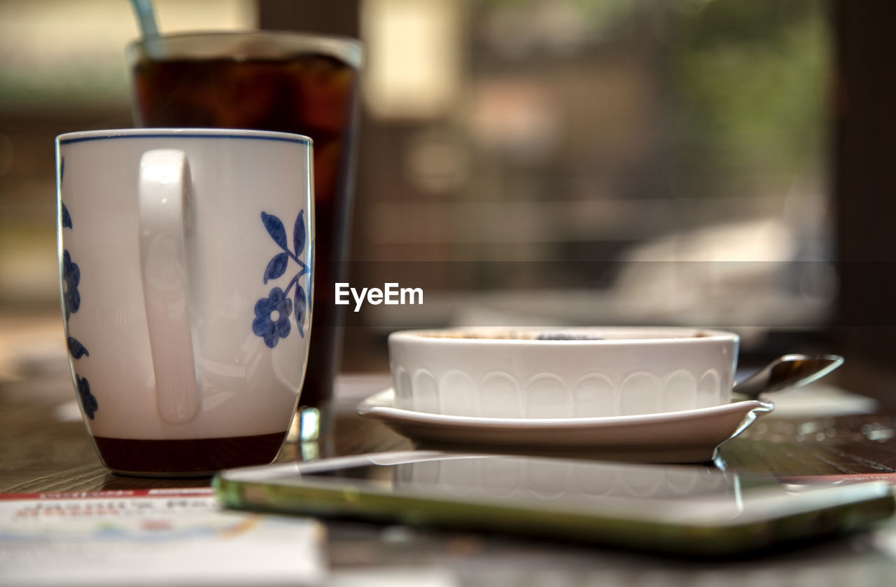 Close-up of bowl and coffee cup with mobile phone on table