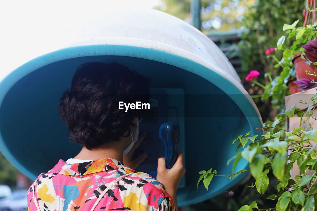 Rear view of woman using telephone booth outdoors